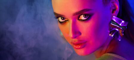 Sexy girl with bright makeup posing in neon light and smoke, looking at camera, free space