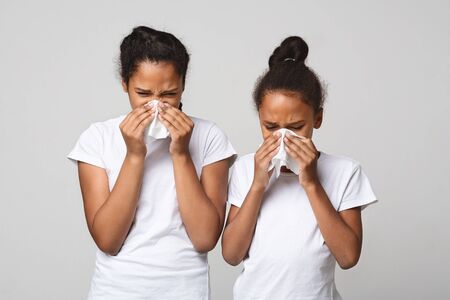 Got sick. Two young african girls blowing noses over grey studio backgroundの写真素材