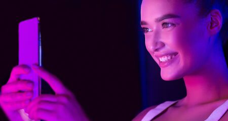 Excited woman taking selfie on phone, face illuminated by pink light in studioの写真素材