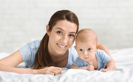 Happy family. Portrait of beautiful single mother and her adorable baby boy lying in bed and looking...
