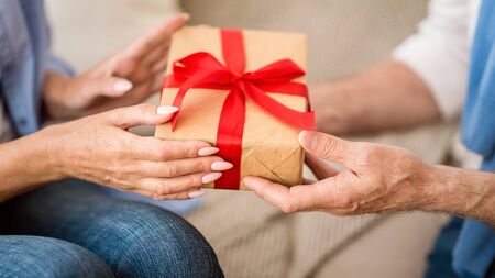 Senior woman giving Christmas gift box to elderly man, celebrating holidays together, closeupの写真素材