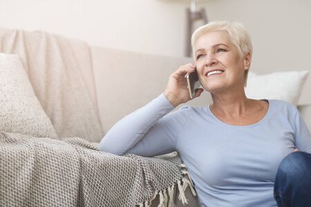 Happy female matured business woman talking by phone, working from home, sitting on floor, cropped, copy spaceの写真素材