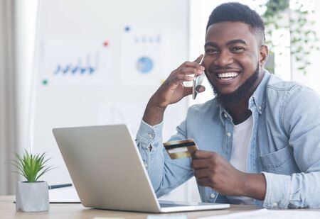 Shopping online. Cheerful african american guy talking on phone to internet shop manager, discussing...