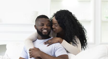 Young african american man and woman embracing on couch at home, enjoying spending time together. Panorama with copy spaceの写真素材