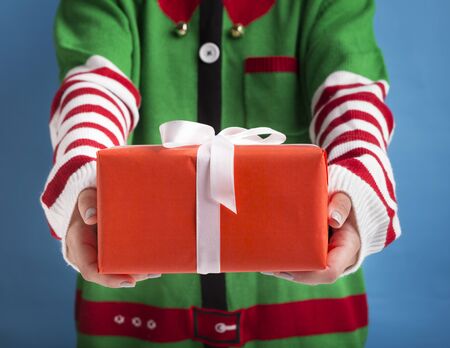 Christmas presents delivery. Santas little helper holding holiday gift with ribbon on background