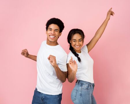 Overjoyed guy and girl dancing and laughing on pink studio background