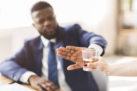 African american businessman saying no to glass of whiskey offered by female colleague, selective focus, copy spaceの写真素材
