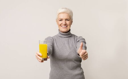 Beautiful senior woman recommending orange juice, showing thumb up to camera. Free spaceの写真素材