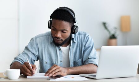 Concentrated african american guy in headphones studying foreign language online through video...