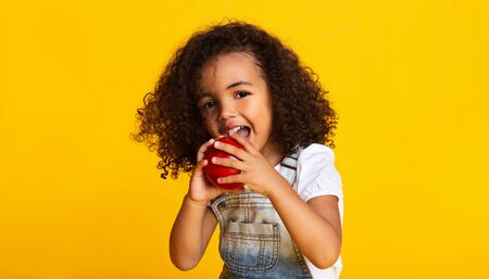 Vitamin snack. Little girl biting red apple over yellow backgroundの写真素材