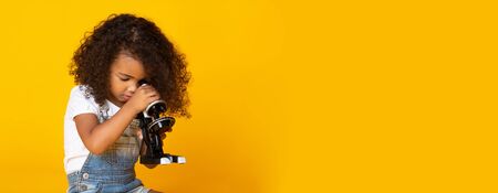Early education concept. Kid girl looking through microscope, yellow background, free space