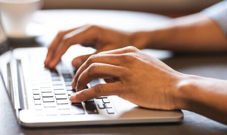 Working with laptop. Close up image of male hands typing text or programming code on laptop at cafe