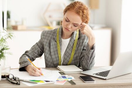 Thoughtful seamstress drawing sketches in dressmaking studio, creating new collection