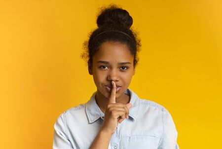 Secret. Beautiful black teen girl put finger on lips, making hush sign