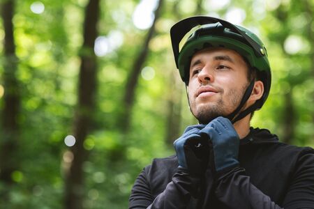 Young handsome man wearing his sport helmet on forest background, close up, copy spaceの写真素材