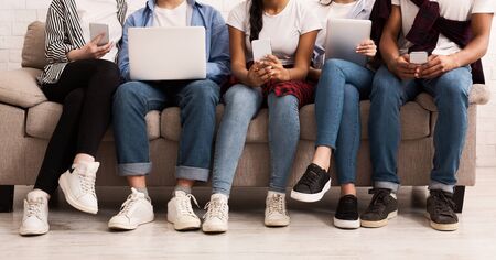 Internet addiction. Friends with gadgets sitting on sofa in living room, cropの写真素材
