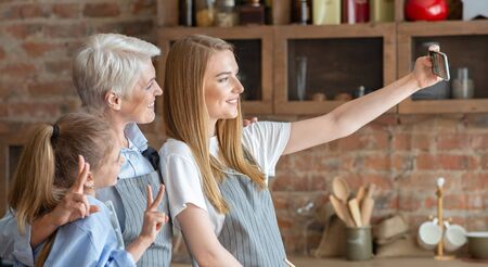 Mother, daughter and grandmother taking selfie at kitchen, side view, panorama with empty space
