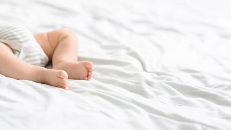 Closeup of tiny legs of newborn baby lying on bed in bodysuit, cropped image with copy spaceの写真素材