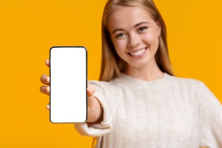 App for education. Cute teenage girl showing blank smartphone screen over orange background with...