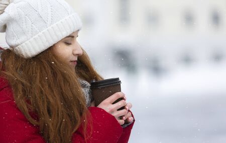 Freezing redhead girl drinking hot coffee during walk on winter day, side view, free spaceの写真素材