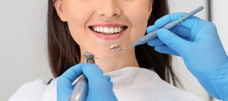 Beautiful smile concept. Smiling young woman attenting dental clinic, hands of dentist with drilling...