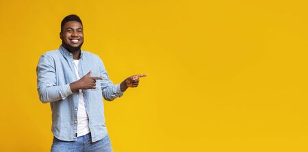 Cool offer. Cheerful african american man pointing two fingers aside at copy space on yellow studioの写真素材