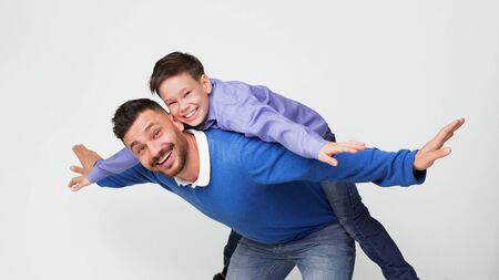 Happy dad and son playing together, man riding boy on back like flying on plane, white panoramaの写真素材