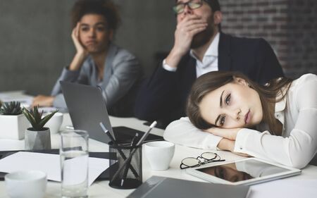 Boring presentation. Young business people looking bored, woman lying on table and looking awayの写真素材