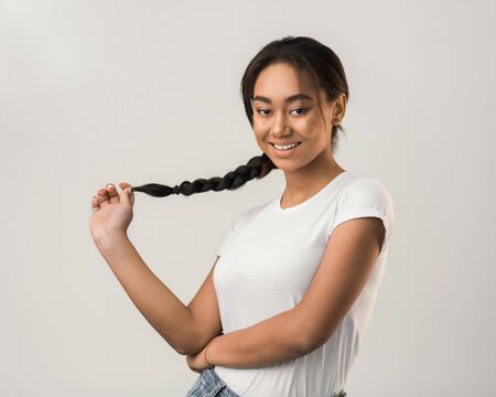 Smiling girl holding pigtail and posing to camera over grey studioの写真素材