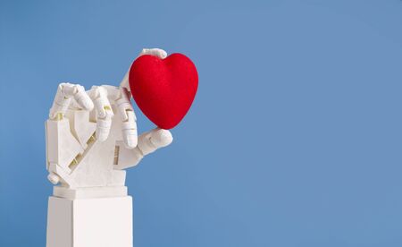 Innovation in cardiology. Robotic doctor hand holding red heart, blue background with copy spaceの写真素材