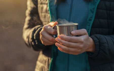 Warm up. Woman holding camping cup with hot drink, croppedの写真素材