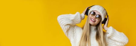 Cheerful woman in winter hat and sunglasses listening to music and dancing, using wireless headset,...