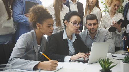 Serious business team analyzing reports on laptop and taking notes at meeting in office