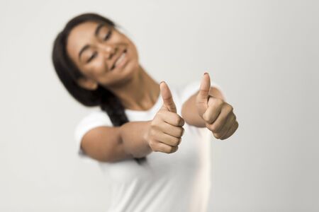Yeah, I like! Happy girl showing thumbs up over grey studio backgroundの写真素材
