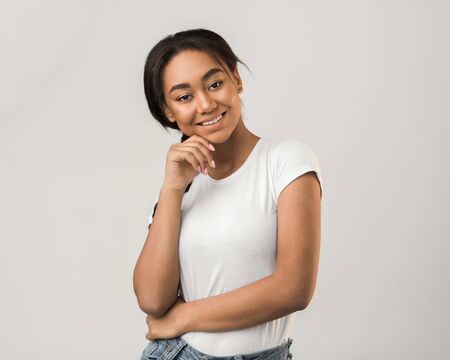 Happy girl posing and touching chin over grey background, smiling to camera, cropの写真素材