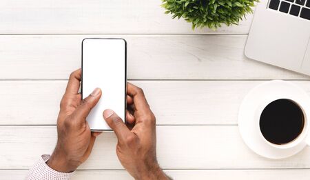 Cool app. Black mans hands holding modern smart phone with blank screen at workplace, top view