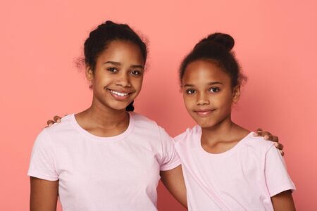 Portrait of two cute little african sisters embracing over pink studio background