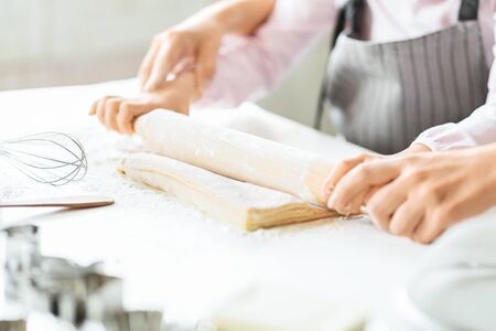 Homemade cooking. Small girl rolling out dough on kitchen table with help of her mom, closeupの写真素材
