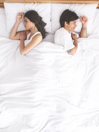 Relationship crisis. Upset couple sleeping separately on their bed, top view, free spaceの写真素材