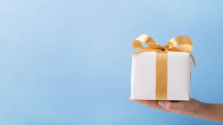 Creative Christmas gift with golden ribbon on woman palm, blue background, copy space, panorama