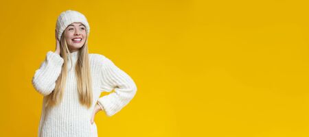 Interested pretty blonde girl in warm white clothes looking at free space, yellow background, panoramaの写真素材