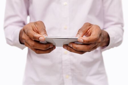 Unrecognizable man holding smartphone in horizontal orientation playing video games over white...