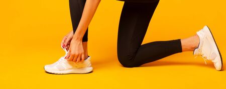 Fitness Fashion. Unrecognizable Girl Lacing Shoes For Workout Over Yellow Background In Studio. Cropped, Panoramaの写真素材