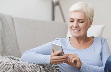 Portrait of modern senior woman using phone at home, copy space
