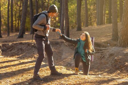 Young handsome hiker helping his girlfriend uphill in the countryside, copy space
