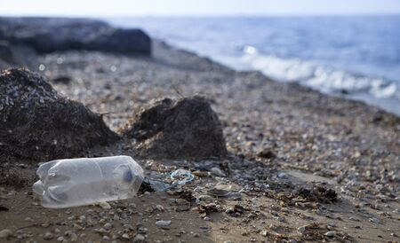Single use plastic bottle discarded on beach next to sea, close up, empty space