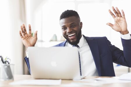 Excited afro businessman expressing joy and happiness in office, got new clients, looking at laptop, copy space