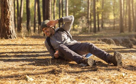 Young man having trouble feeling knee pain during travel in forest. Health problem in journey, copy spaceの写真素材