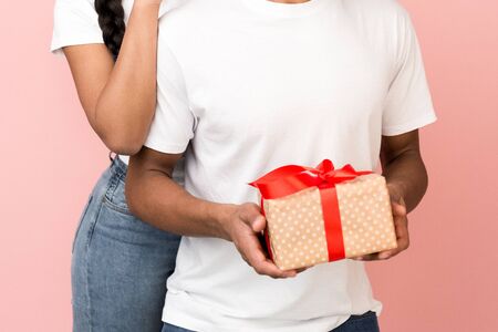 Surprise concept. Girl giving gift to boyfriend from behind, pink background, cropの写真素材