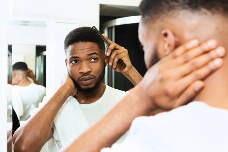Young african man combing his hair in bathroom, looking at mirrorの写真素材